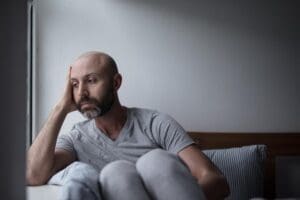 bald man leans his head on his hand while sitting on a couch and wonders how to honor your emotions