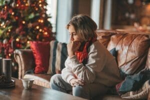a distraught woman sits on her couch and leans forward while thinking how she will conquer holiday stress