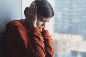 woman sits near a window and holds her hands to her ears experiencing one of her ptsd triggers