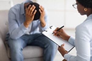 man sits in a chair slumped and resting his hands in his hands while his doctor explains complex ptsd