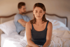 a woman experiencing relationship ocd sits on the edge of her bed while her husband lays down