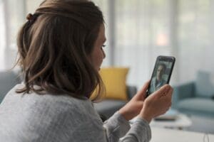 woman holds her phone up while using the options for telehealth for her anxiety treatment
