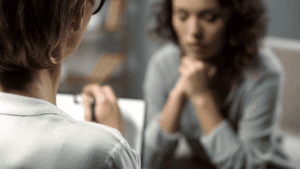 a therapist takes notes as a woman patient sits across from her and lists her tms therapy side effects