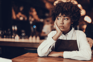 a sad looking woman sits at a table with her hand resting on the side of her face wondering the signs of high-functioning depression