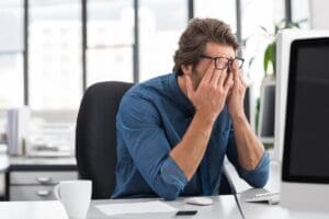 an upset man covers his face while sitting at his desk and wondering how does depression affect the brain