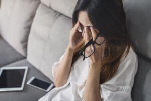 woman with long hair sits on couch and covers her eyes struggling with processing trauma