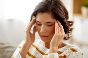 a woman with short brown hair holds her hands to both temples and asks herself what is chronic stress