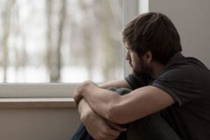 man sit near window and look out the window and experiencing signs of grief and depression