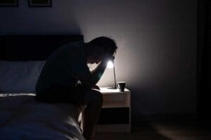 a person sits on their bed in the dark struggling with depression at night