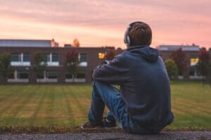 a teen with headphones sits on a football field thinking about his defiant behavior and how to address it