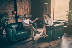 two people sit near each other on a couch and chair discussing behavioral activation therapy