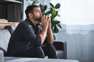distraught man sits on a couch thinking about how to find a anxiety therapy in pittsburgh
